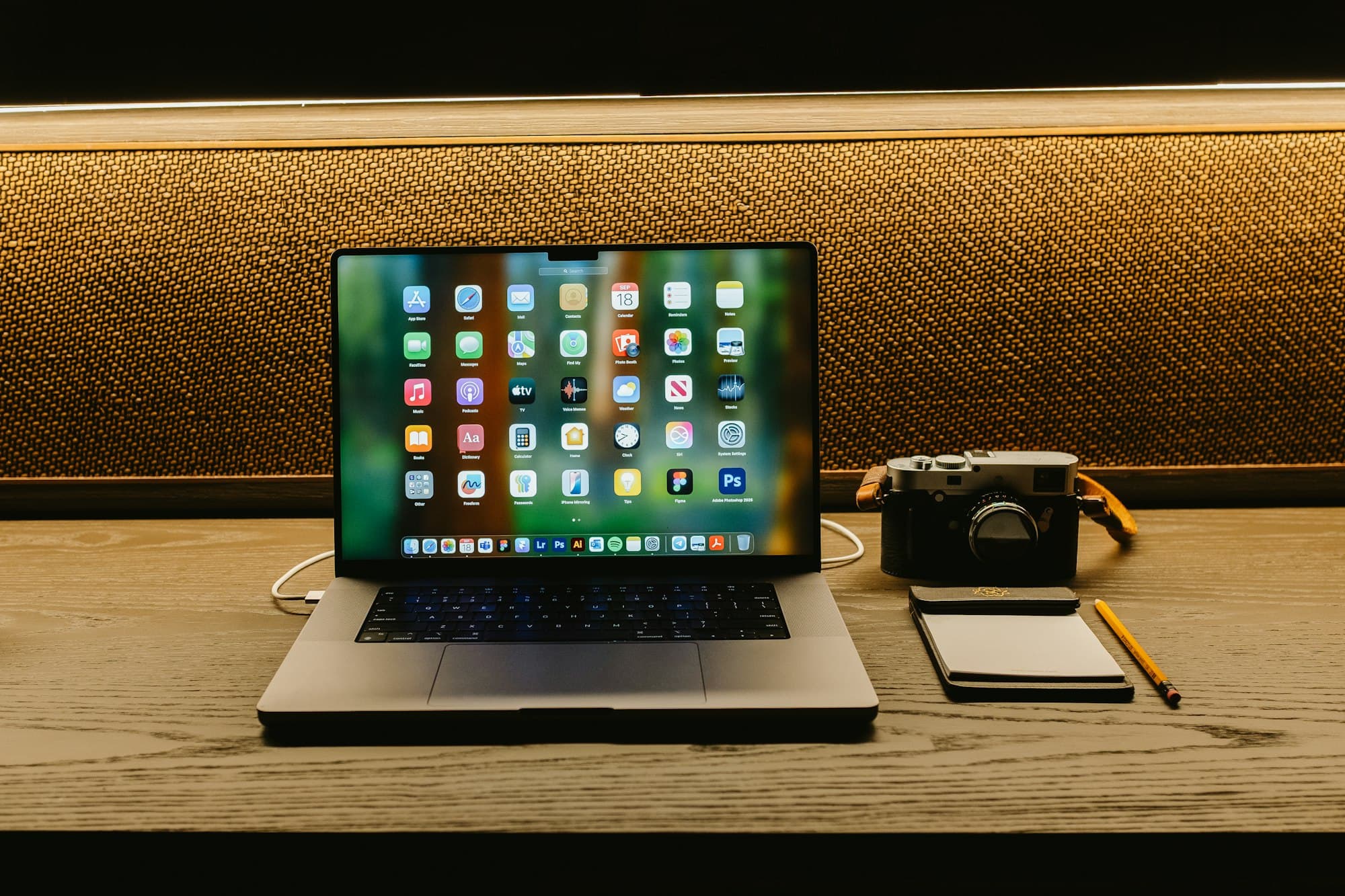 A laptop, camera, and notebook laid out on a wooden desk